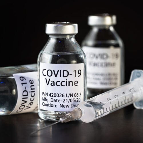 Coronavirus Covid-19 vaccine concept -  three glass vials on black table, hypodermic syringe needle near, closeup detail (label own design - dummy data, not real product)