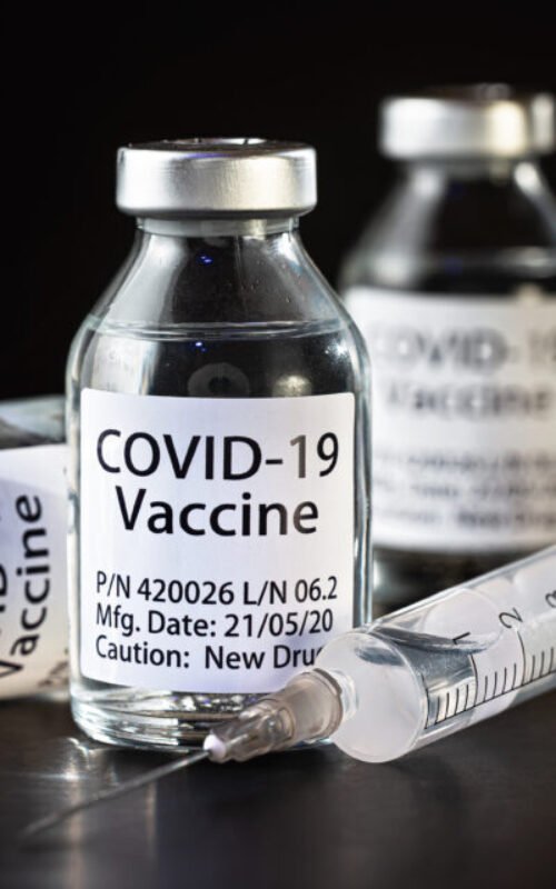 Coronavirus Covid-19 vaccine concept -  three glass vials on black table, hypodermic syringe needle near, closeup detail (label own design - dummy data, not real product)